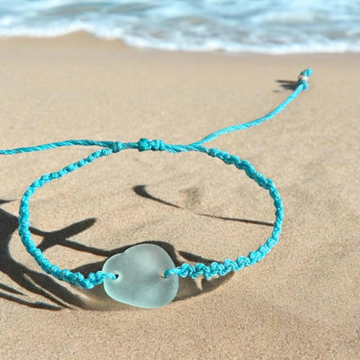 Handmade macrame sea glass bracelet with adjustable seafoam cord on beach sand background