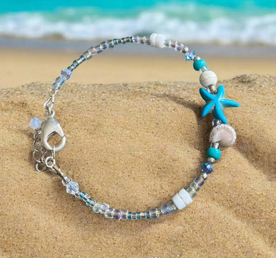 Starfish charm bracelet with blue, white, and silver beads on sandy beach background